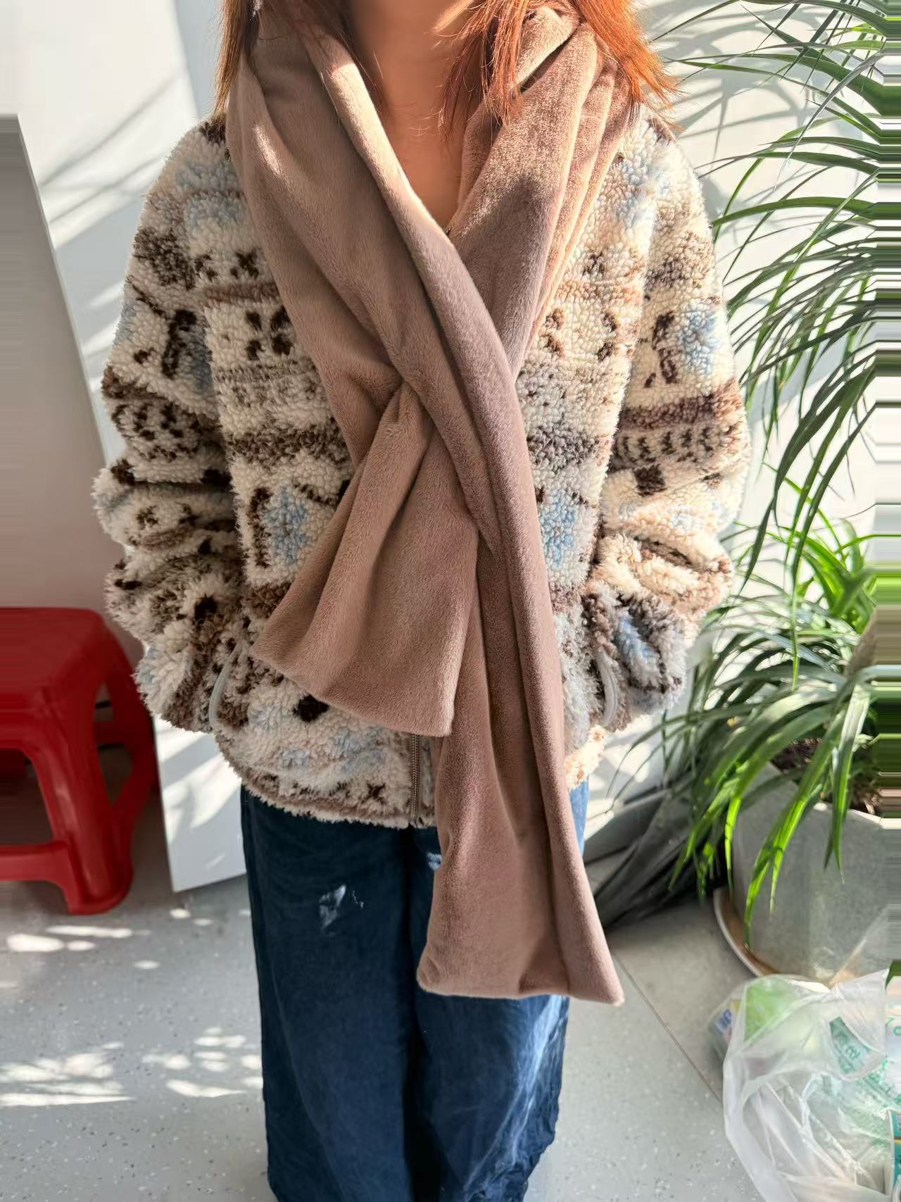 Person wearing a patterned coat and beige scarf indoors with plants in the background