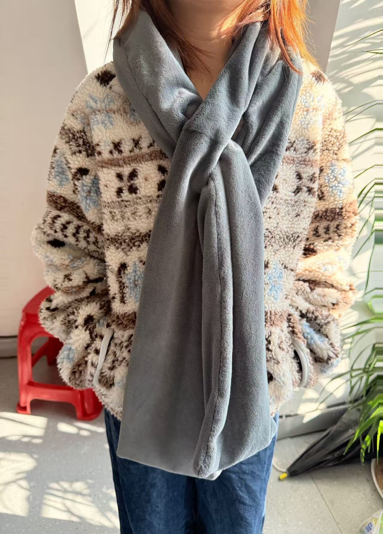 Person wearing a patterned sweater and gray scarf with a blurred background