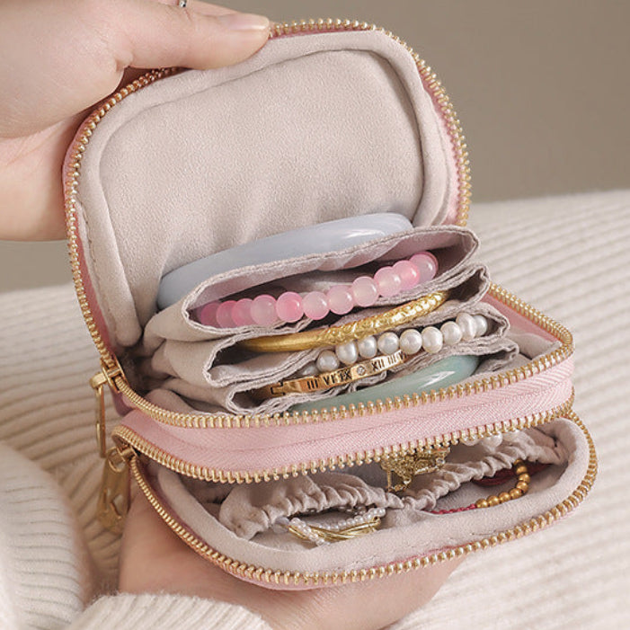 Hand holding a pink jewelry organizer with jewelry inside, on a neutral background.