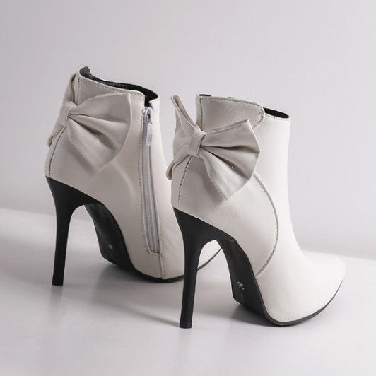 White high-heeled boots with bow details on a light gray background