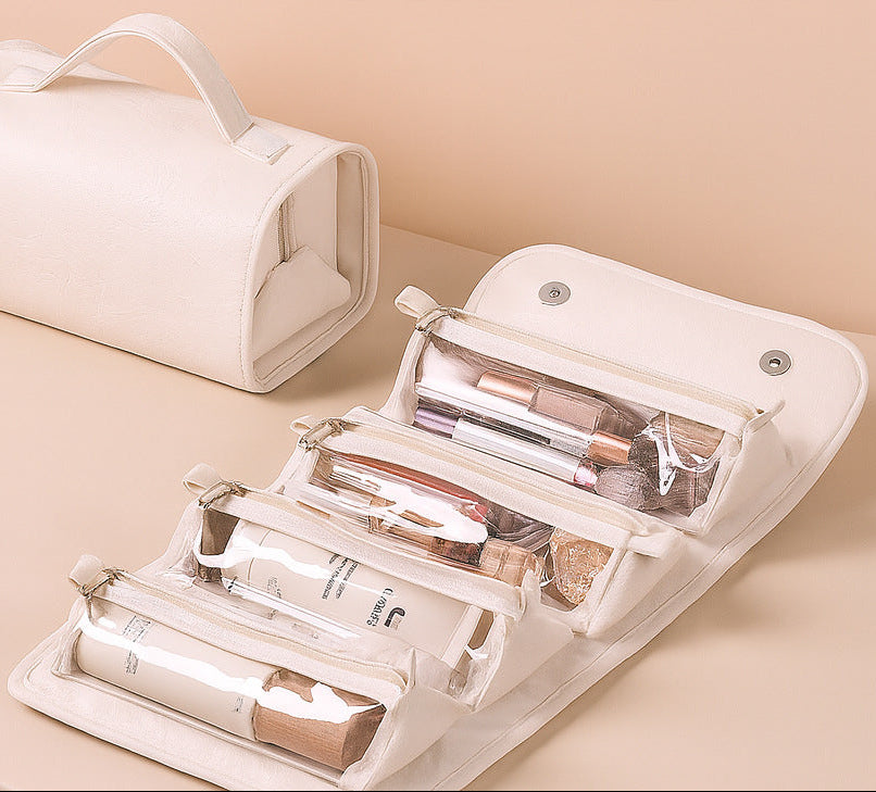 An off-white travel makeup bag set shown on a beige surface, with one closed bag and one open bag displaying multiple clear zip compartments filled with cosmetics.