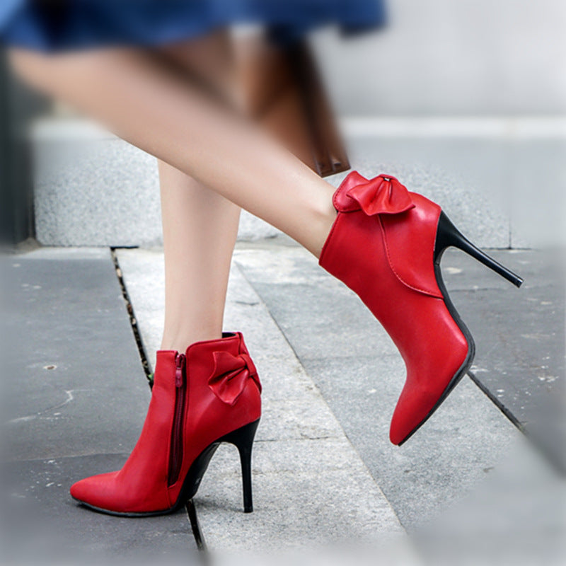 Red high-heeled shoes with bows worn by a person on a sidewalk.