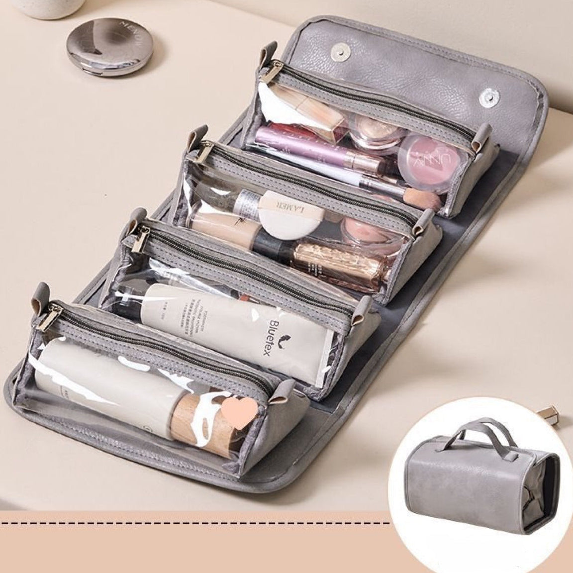 Gray cosmetic bag with makeup items on a beige surface. Shown both open and closed.