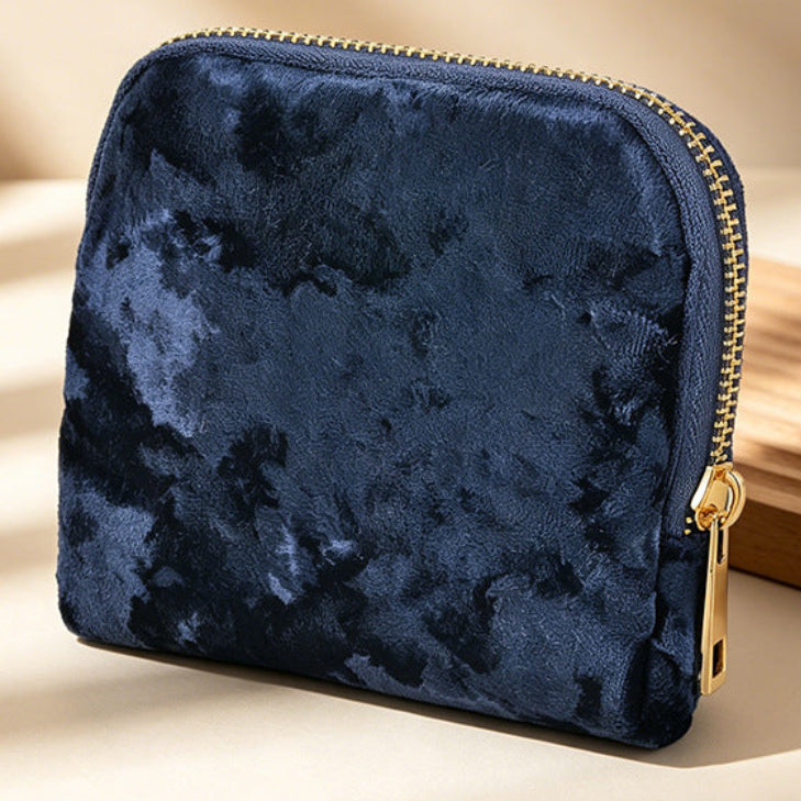 Blue crushed velvet looking pouch with gold zipper on a beige background