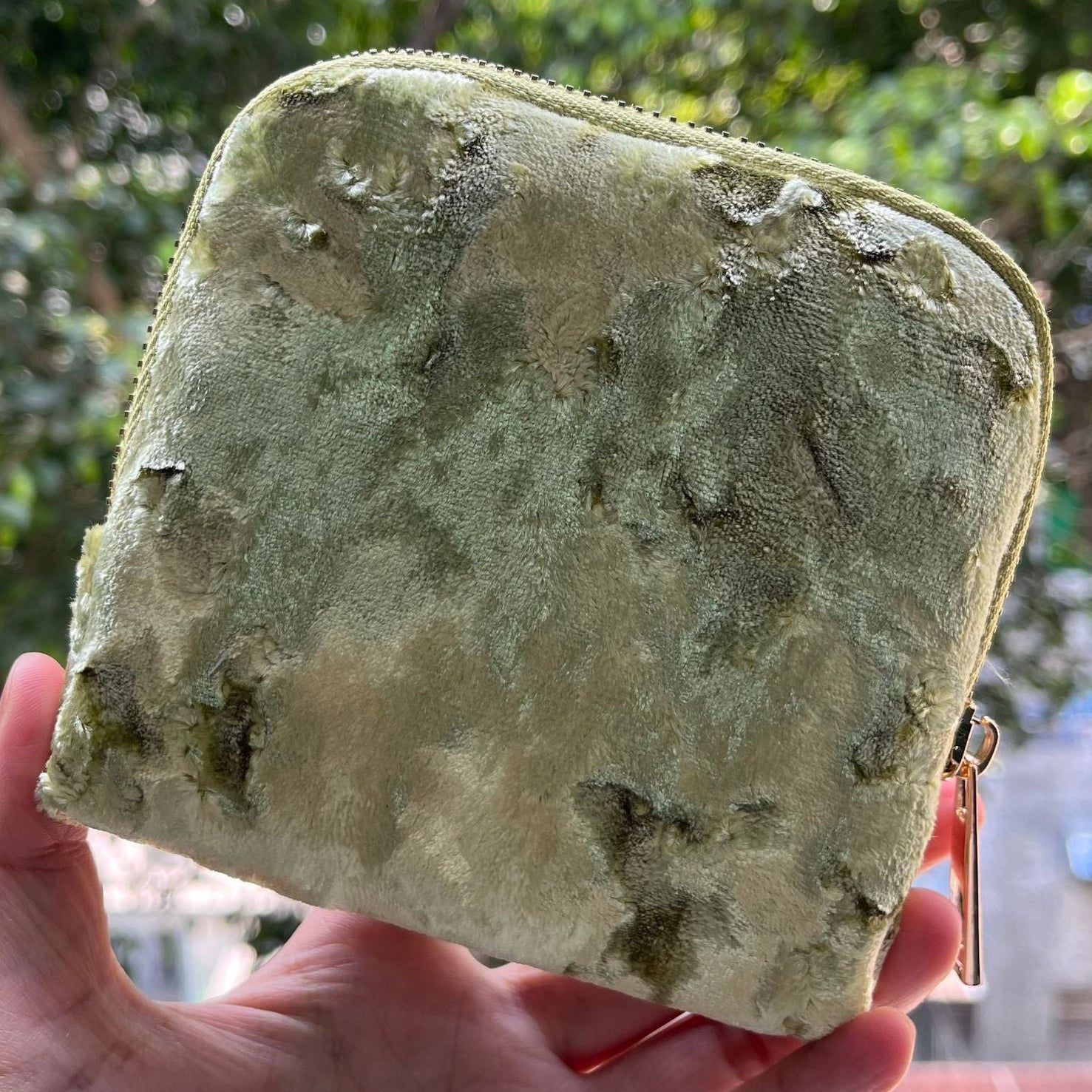 Mossy green jewellery pouch held in front of a blurred green outdoor background
