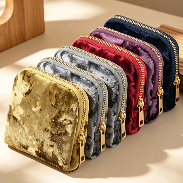 Row of colourful crushed velvet looking jewellery travel pouches with gold zippers on a light surface.