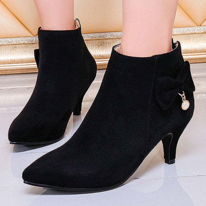 Black ankle boots with a bow detail on a reflective floor.