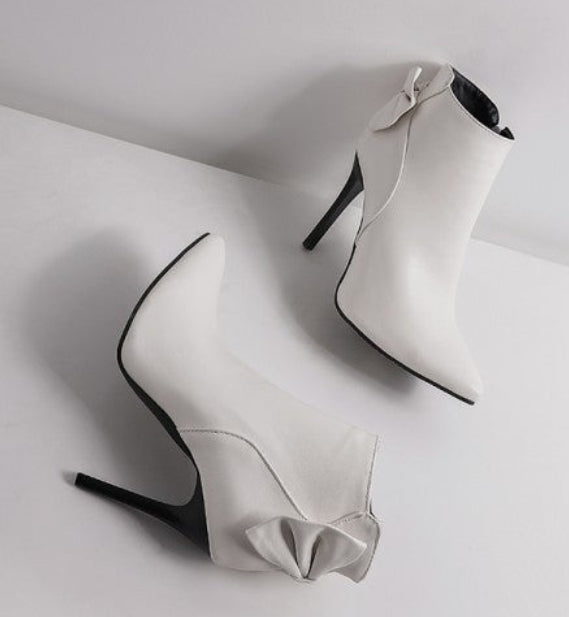White high-heeled shoes with bow details on a light gray background