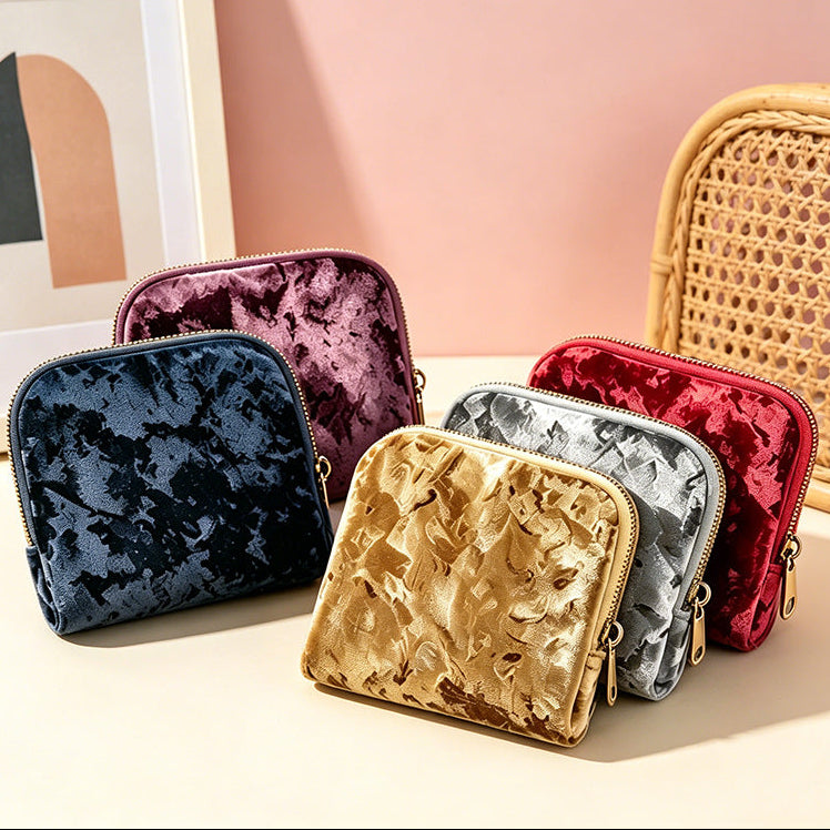 Set of colorful velvet pouches on a light surface with a pink wall and framed picture in the background.