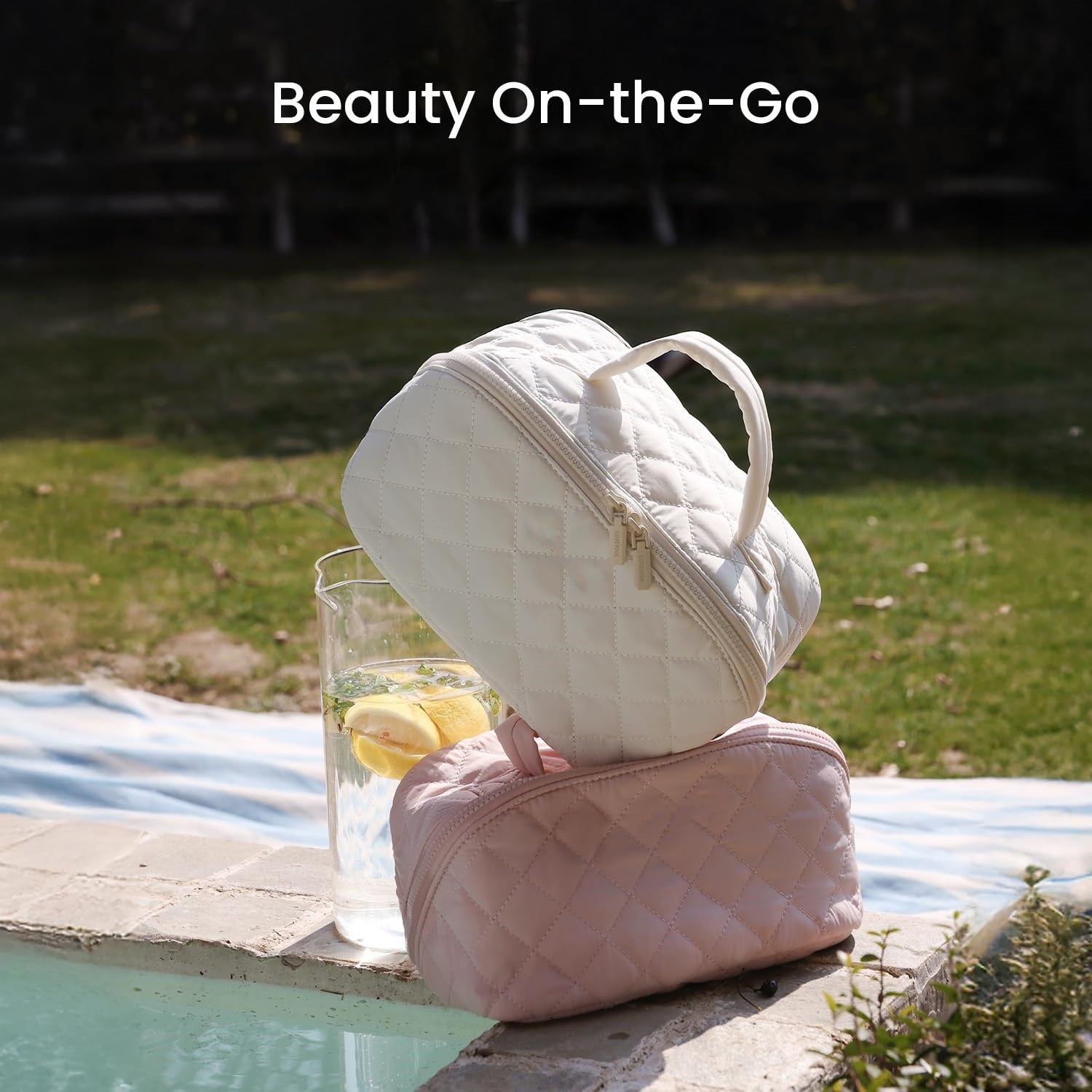 Quilted white and pink cosmetic bags by a poolside with a glass of lemon water.
