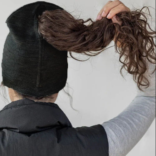 Person wearing a black beanie and gray vest, holding their hair up.