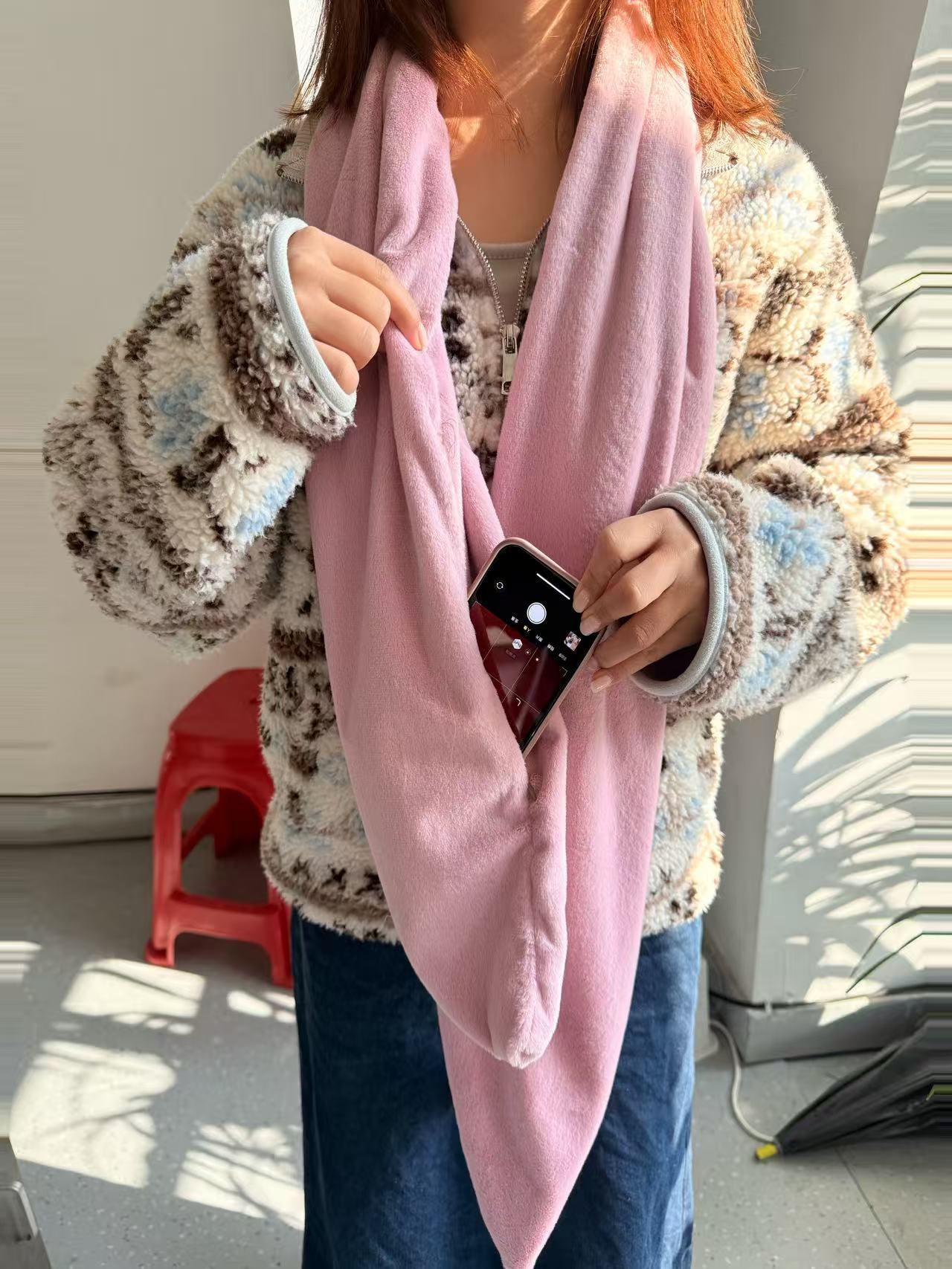 Person holding a pink scarf showing it's secret pocket wearing a patterned jacket and jeans indoors.